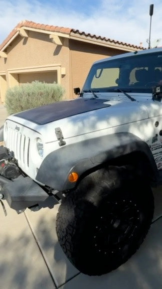 White Jeep with a hood-mounted solar panel parked in partial sunlight